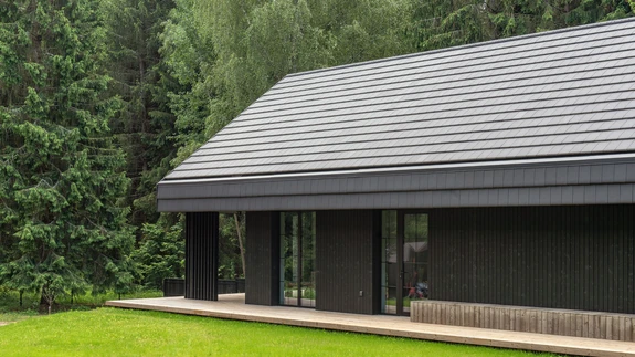 Lihtsa vormi ja tumeda fassaadiga hoone asub lummava looduse keskel.