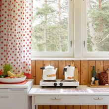 Väike elektripliit «kaheraudne» on suvilasse piisav. Armsad kardinad ja punaseks värvitud taburetid lisavad särtsu.